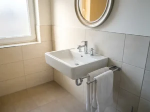 Schone moderne badkamer in arbeidersverblijf met witte keramische wastafel, chromen kranen en netjes gevouwen handdoeken op een gepolijst rek.