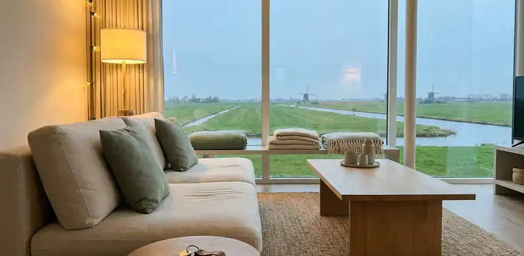 Moderne woonkamer met Scandinavisch meubilair, sleutels op houten bijzettafel en uitzicht op Nederlands polderlandschap.