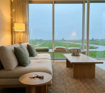 Moderne woonkamer met Scandinavisch meubilair, sleutels op houten bijzettafel en uitzicht op Nederlands polderlandschap.
